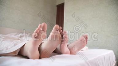 一对年轻夫妇的脚从卧室的被子下伸出来。 两只赤脚互相抚摸